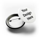 Mockup of a round white button pin featuring black 'Your Design Here' text on the front and an open back with pin mechanism, illustrating customizable badge printing.