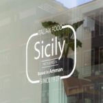 Shopfront window sticker mockup with white outline and text reading 'Italian Food Sicily, pasta & pizza, based in Amman since 1927', ideal for custom restaurant window decals.