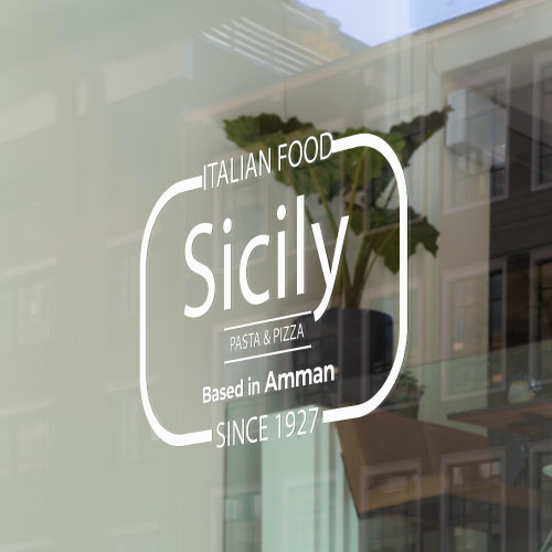 Shopfront window sticker mockup with white outline and text reading 'Italian Food Sicily, pasta & pizza, based in Amman since 1927', ideal for custom restaurant window decals.