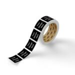 Roll of black sticker labels featuring repeated 'Your Design Here' design on squares, demonstrating customizable tape or label printing for branding.